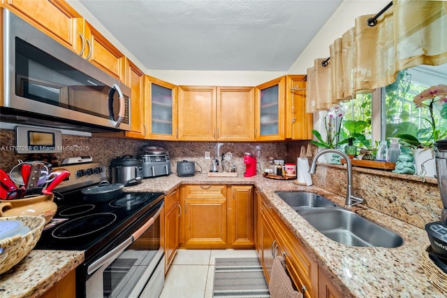 kitchen featuring backsplash, light tile patterned floors, appliances with stainless steel finishes, and a sink