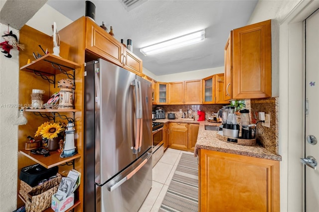 kitchen with glass insert cabinets, light tile patterned floors, light stone counters, backsplash, and stainless steel appliances
