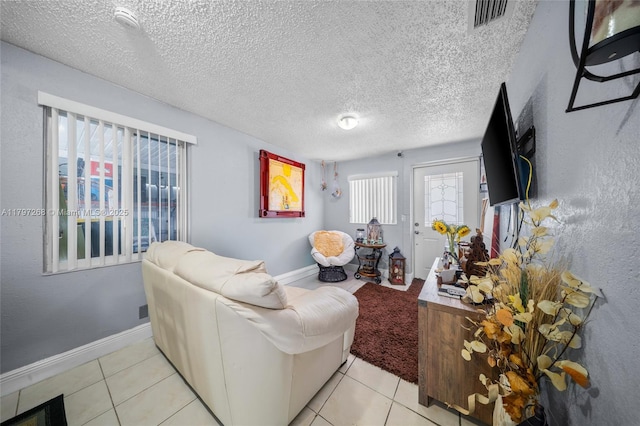 living area with baseboards, light tile patterned flooring, visible vents, and a textured ceiling