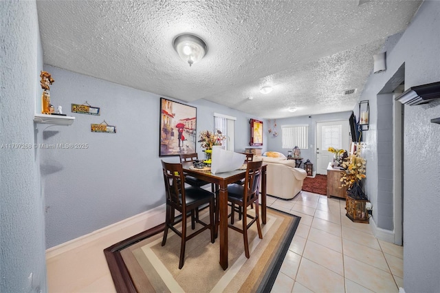 dining area featuring light tile patterned floors, baseboards, visible vents, and a textured ceiling