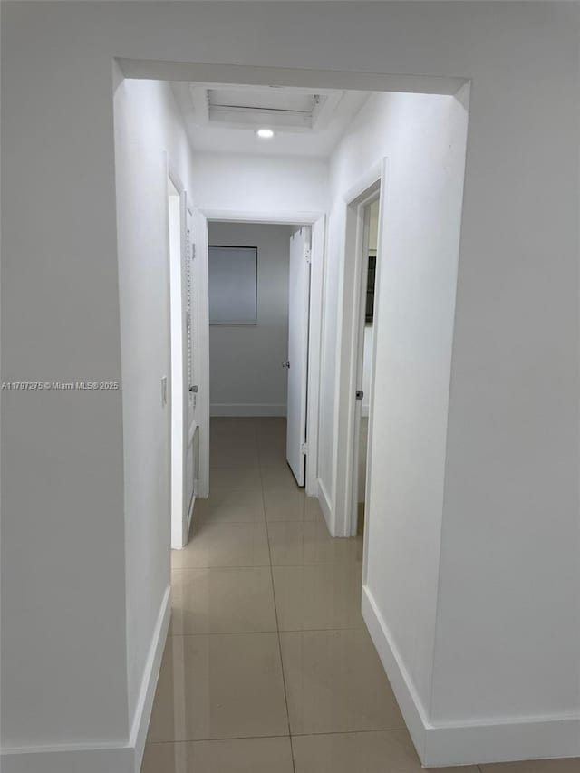 corridor with baseboards, attic access, a tray ceiling, and light tile patterned floors