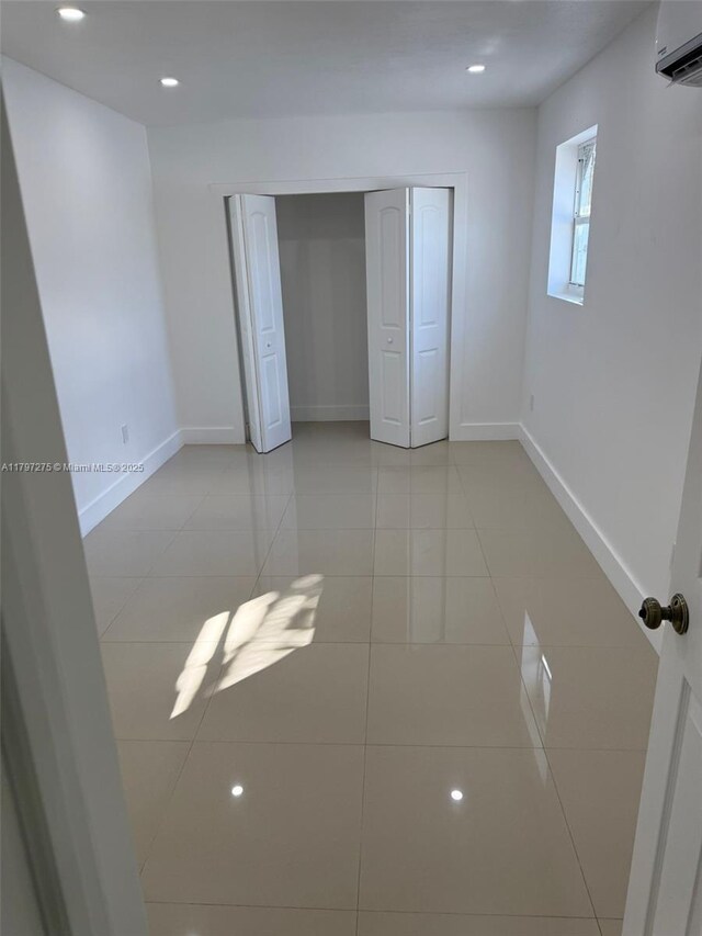 unfurnished bedroom with baseboards, light tile patterned flooring, a wall mounted AC, recessed lighting, and a closet