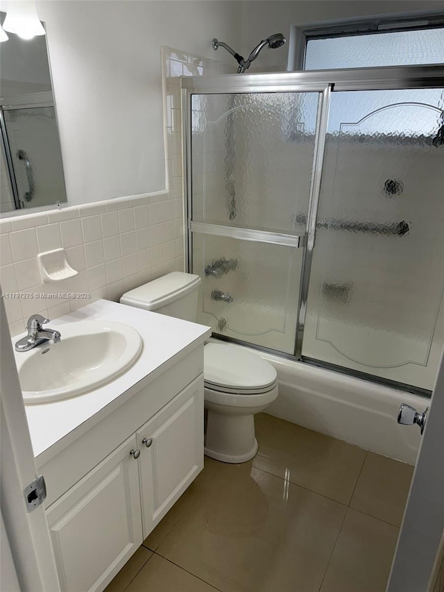 full bathroom featuring tile walls, tile patterned flooring, shower / bath combination with glass door, vanity, and toilet