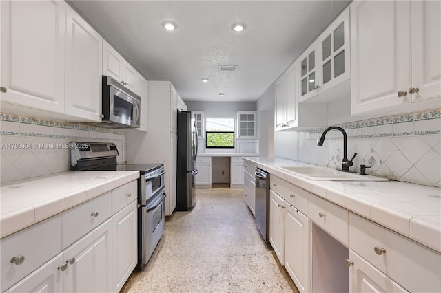 kitchen featuring glass insert cabinets, a sink, white cabinetry, decorative backsplash, and appliances with stainless steel finishes