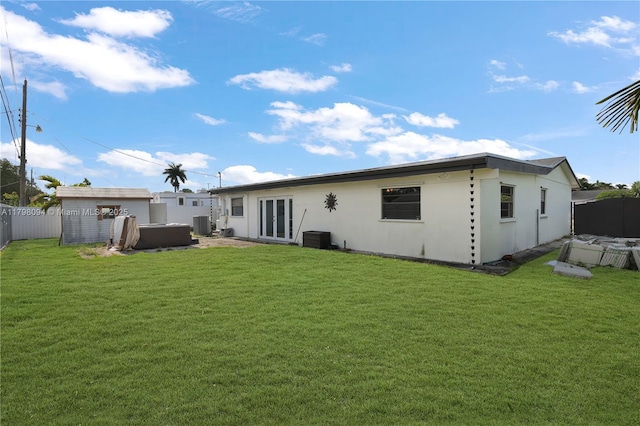 back of house with a lawn, a jacuzzi, central AC, stucco siding, and a fenced backyard