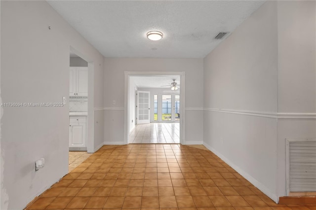 empty room featuring a textured ceiling, visible vents, light tile patterned floors, and ceiling fan