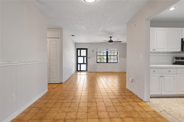 interior space with a textured ceiling, white cabinetry, ceiling fan, electric stove, and tile countertops