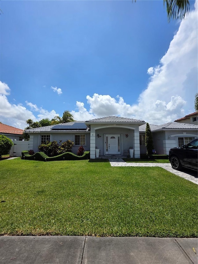 single story home with a front lawn, stucco siding, a tile roof, and solar panels