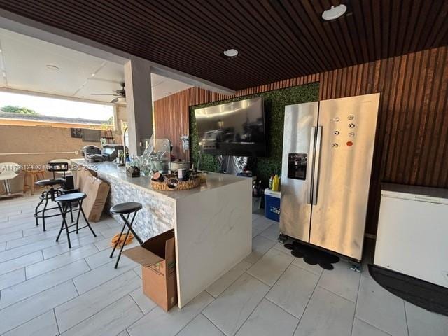 224 E 42nd St, Hialeah, FL 33013 - kitchen featuring stainless steel fridge, wooden walls, ceiling fan, a kitchen breakfast bar, and a peninsula