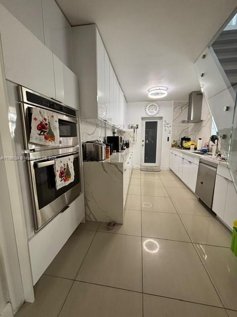 224 E 42nd St, Hialeah, FL 33013 - kitchen with wall chimney exhaust hood, light tile patterned floors, white cabinets, and stainless steel appliances