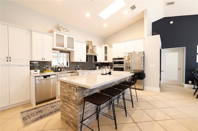 kitchen featuring a kitchen island, wall chimney range hood, appliances with stainless steel finishes, and visible vents