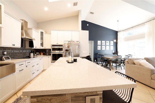 kitchen with stainless steel appliances, high vaulted ceiling, visible vents, wall chimney exhaust hood, and a kitchen island