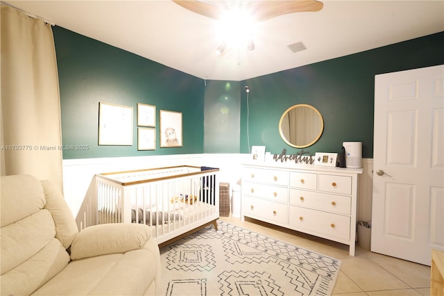 bedroom featuring wainscoting, ceiling fan, a nursery area, and tile patterned floors