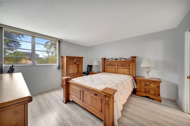 bedroom with a textured ceiling, baseboards, and light wood-style flooring
