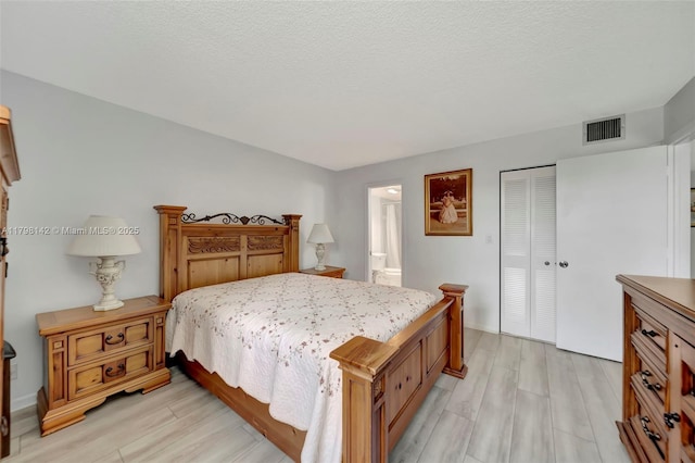 bedroom featuring a closet, visible vents, light wood-type flooring, and ensuite bath