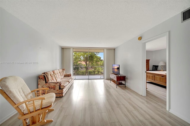 sitting room with a textured ceiling, visible vents, light wood finished floors, a wall of windows, and baseboards