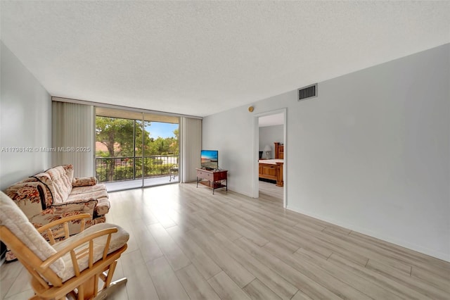 sitting room with light wood-style floors, a wall of windows, visible vents, and a textured ceiling