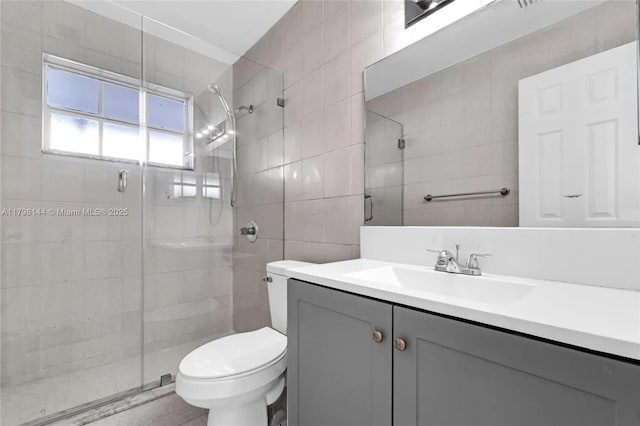 bathroom with tile walls, a shower stall, toilet, and vanity