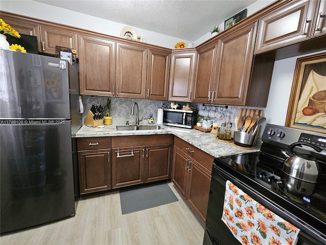 kitchen featuring freestanding refrigerator, light wood-style flooring, a sink, stainless steel microwave, and black electric range
