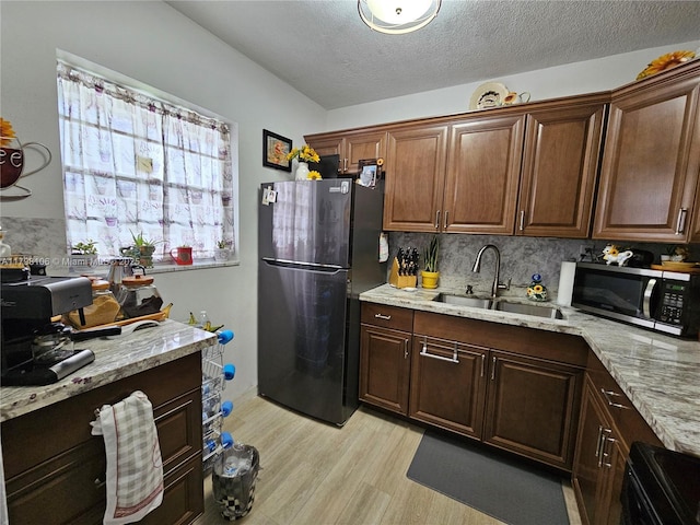 kitchen with light stone countertops, a sink, backsplash, light wood-style floors, and appliances with stainless steel finishes