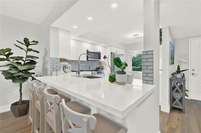 kitchen with a peninsula, light wood-type flooring, stainless steel appliances, and backsplash