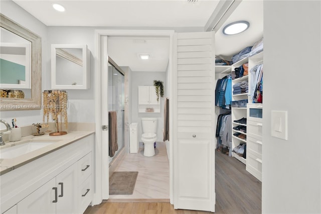 full bathroom with toilet, wood finished floors, a stall shower, a walk in closet, and vanity