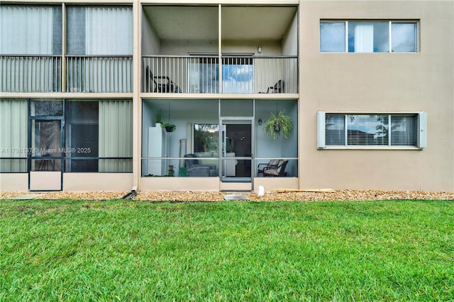 rear view of property featuring a yard, stucco siding, and a balcony