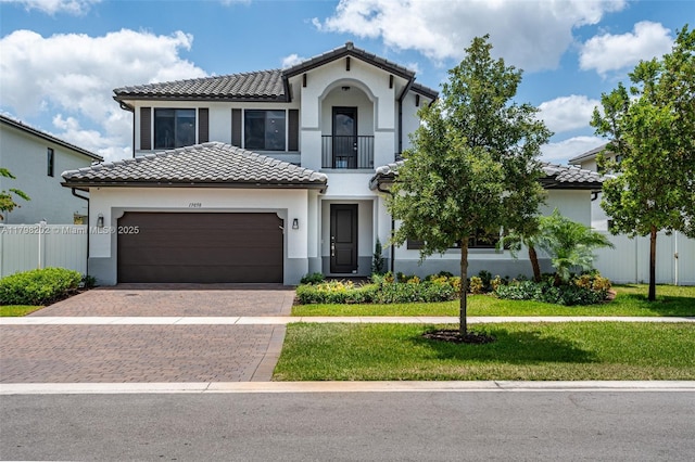 mediterranean / spanish house featuring a tile roof, fence, a front yard, and a balcony