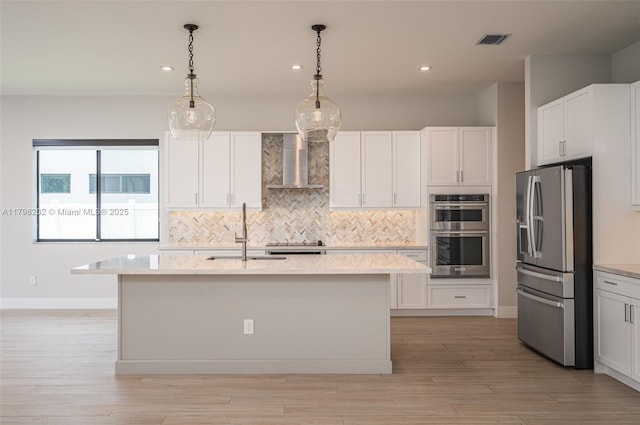 kitchen with a sink, stainless steel appliances, wall chimney range hood, visible vents, and decorative backsplash