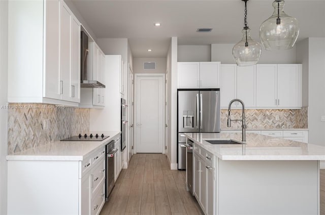 kitchen with a sink, wall chimney range hood, white cabinetry, and visible vents