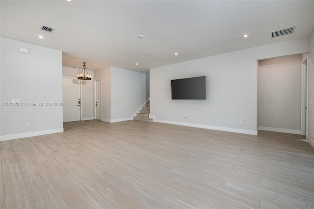 unfurnished living room featuring baseboards, light wood-style floors, an inviting chandelier, and visible vents