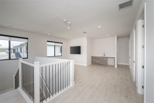 hall with an upstairs landing, light wood-style flooring, visible vents, and recessed lighting