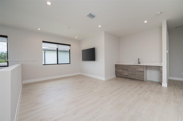 unfurnished living room featuring a sink, light wood finished floors, baseboards, and recessed lighting