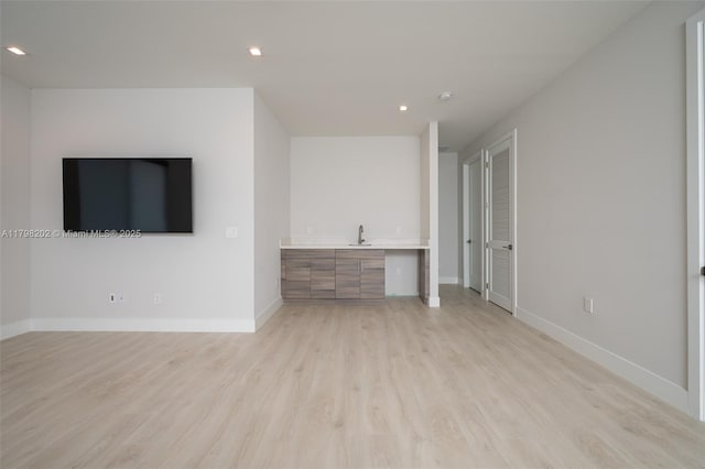 unfurnished living room featuring light wood-type flooring, baseboards, a sink, and recessed lighting