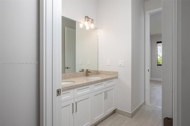 bathroom with baseboards, tile patterned floors, double vanity, and a sink