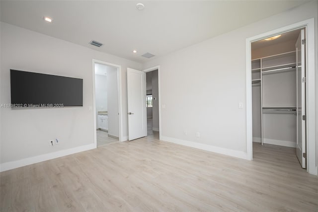 unfurnished bedroom featuring a closet, baseboards, visible vents, wood finished floors, and a spacious closet