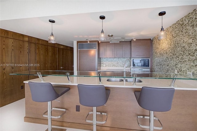kitchen featuring built in appliances, a sink, decorative backsplash, and a kitchen breakfast bar