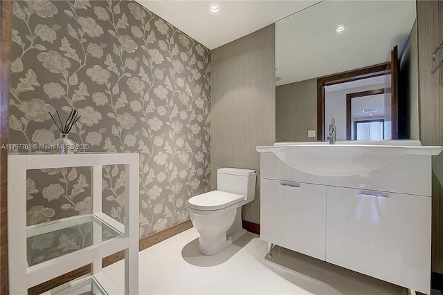 bathroom with toilet, wallpapered walls, and vanity