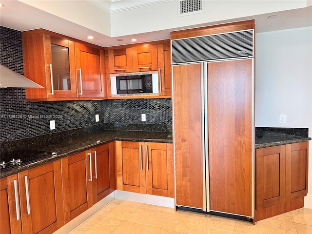 kitchen with brown cabinets, dark stone countertops, crown molding, visible vents, and black appliances