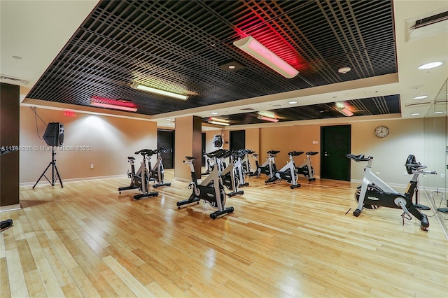 gym featuring baseboards, a raised ceiling, and hardwood / wood-style floors
