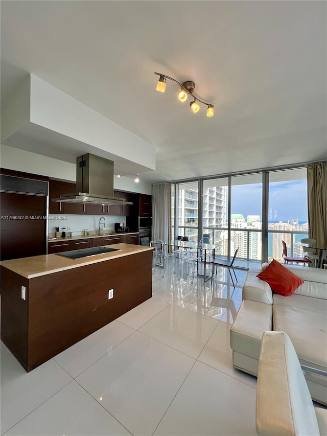 kitchen with island exhaust hood, light tile patterned floors, light countertops, dark brown cabinetry, and a sink