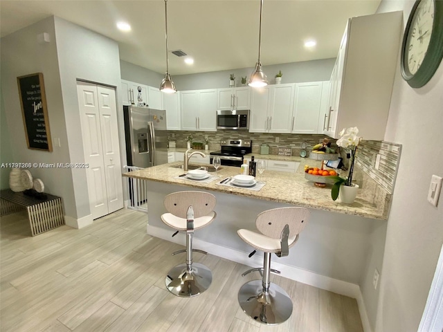 kitchen featuring stainless steel appliances, a peninsula, tasteful backsplash, light stone countertops, and recessed lighting