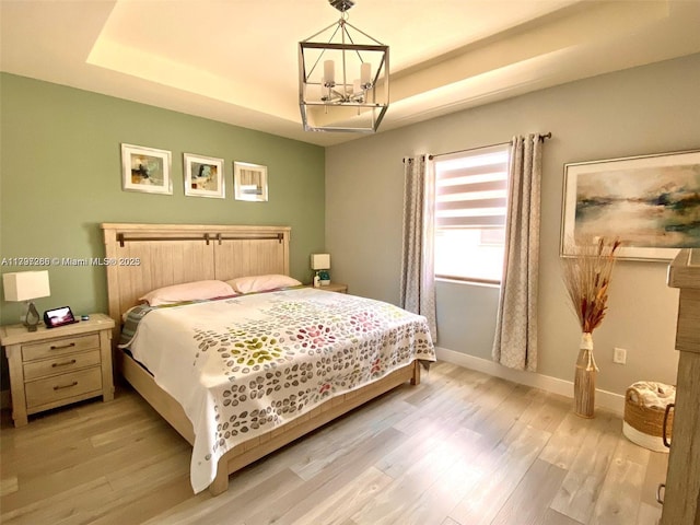 bedroom featuring a chandelier, a tray ceiling, and light wood-style flooring