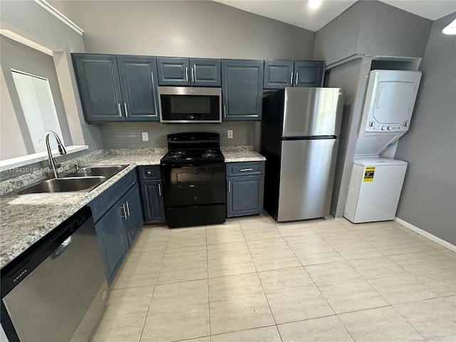 kitchen with appliances with stainless steel finishes, estacked washer and dryer, a sink, light tile patterned floors, and vaulted ceiling