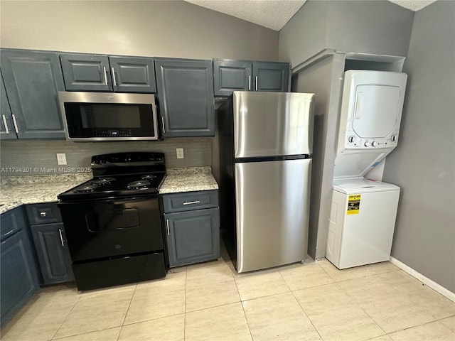 kitchen with stainless steel appliances, estacked washer and dryer, light tile patterned floors, vaulted ceiling, and gray cabinetry
