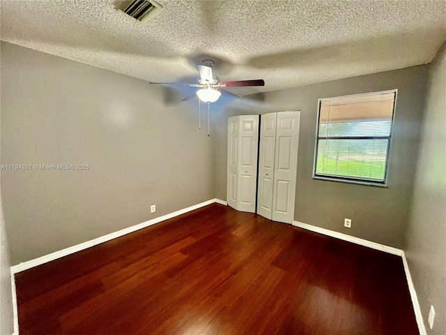 unfurnished bedroom featuring dark wood-style flooring, baseboards, a textured ceiling, a closet, and a ceiling fan
