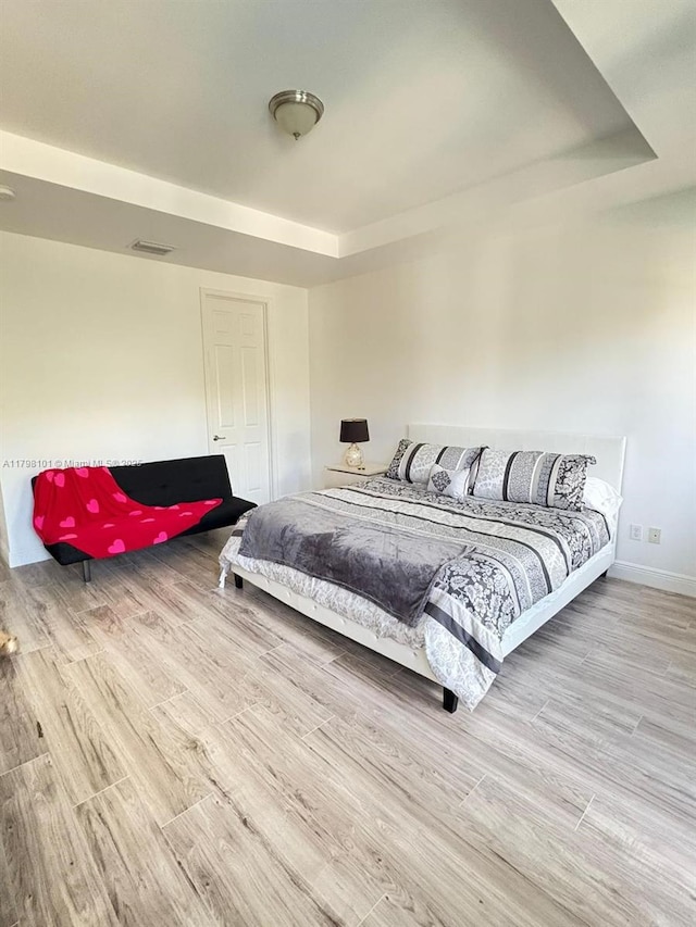 bedroom with wood finished floors, baseboards, and a tray ceiling