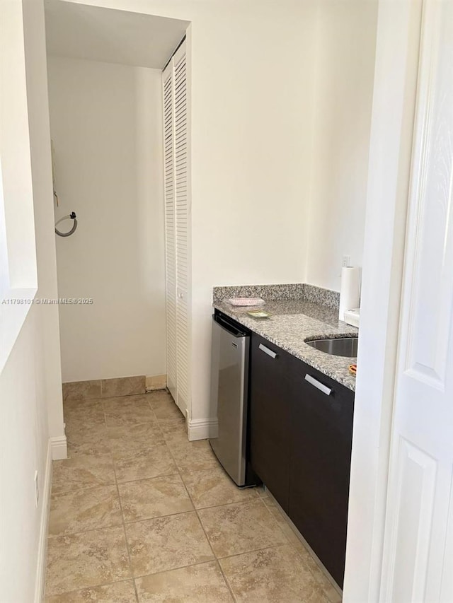 kitchen with fridge, light stone countertops, baseboards, a sink, and dark cabinetry