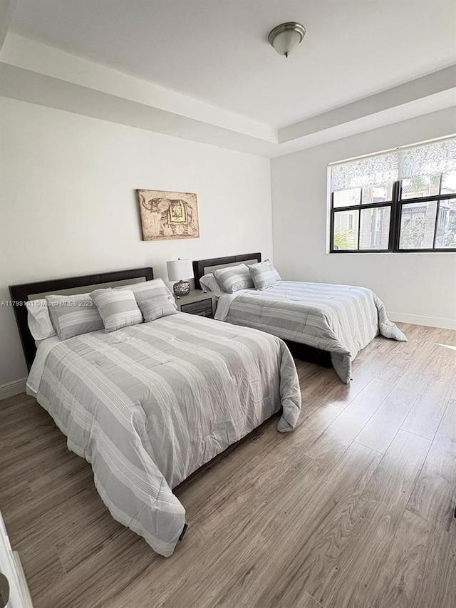 bedroom with wood finished floors, a tray ceiling, and baseboards