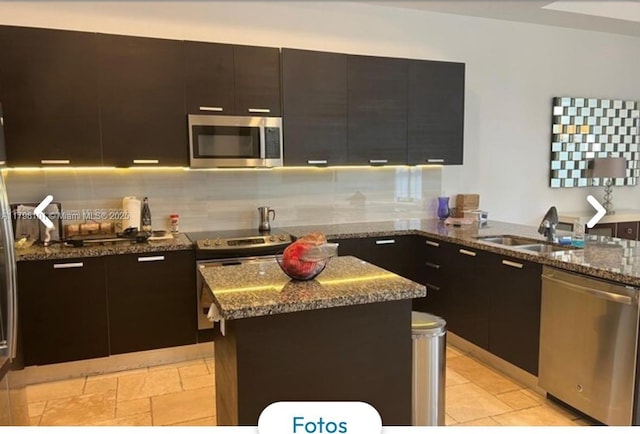 kitchen with stainless steel appliances, a kitchen island, dark stone countertops, and a sink
